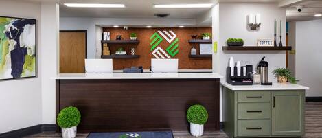 A reception area with a wooden reception desk, a coffee station, and a wall-mounted plant.