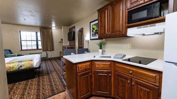 A compact kitchen with wooden cabinets, a microwave, a sink, and a refrigerator. - Extended Stay Airport (Green Bay)