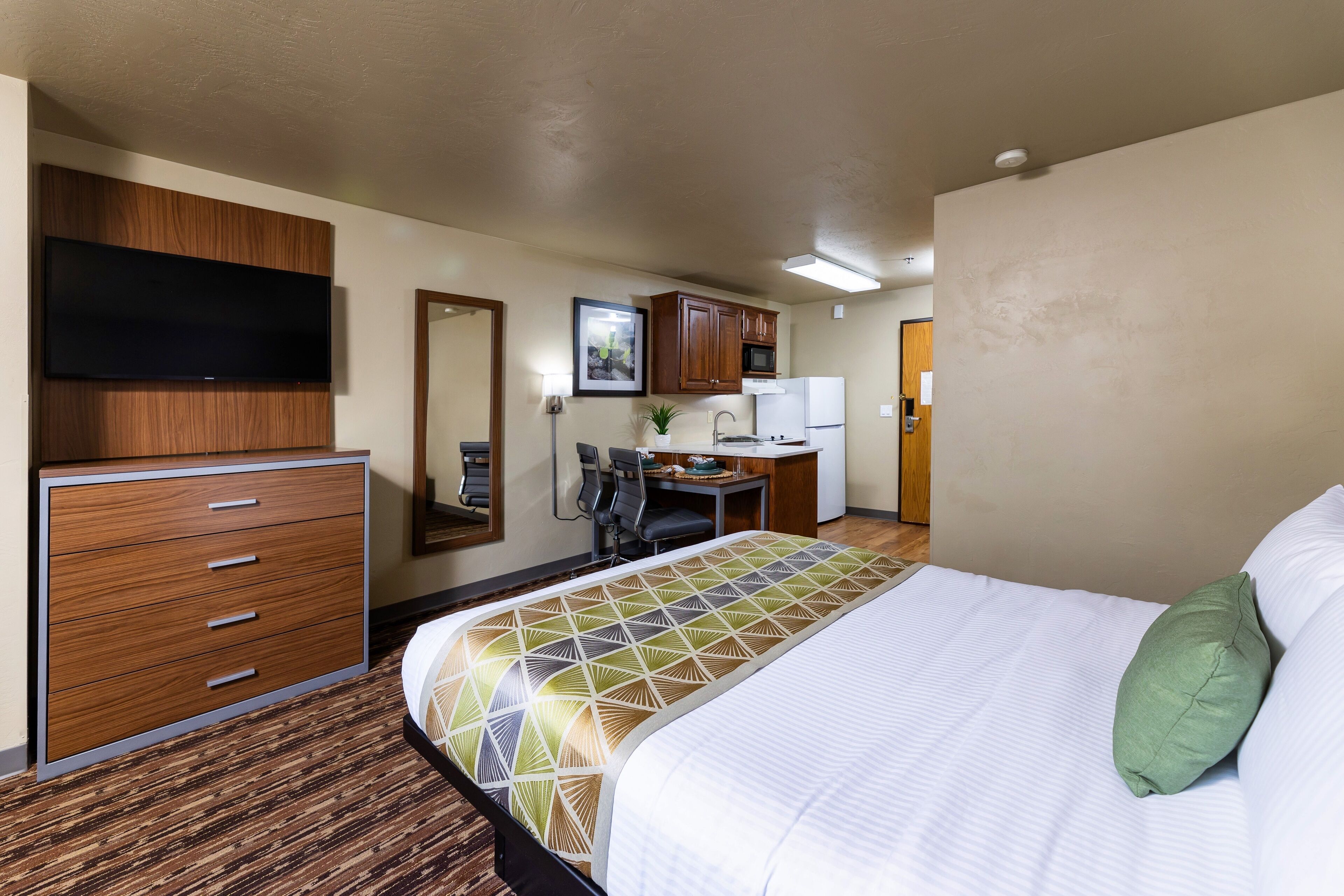 Une chambre d’hôtel équipée d’un lit, d’un bureau, d’une chaise, d’une télévision et d’une kitchenette.
