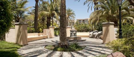 Un patio empedrado con palmeras, una fuente y un edificio al fondo.