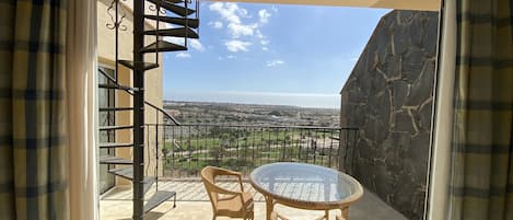 A balcony with a glass table and chairs, a spiral staircase, and a stone wall.