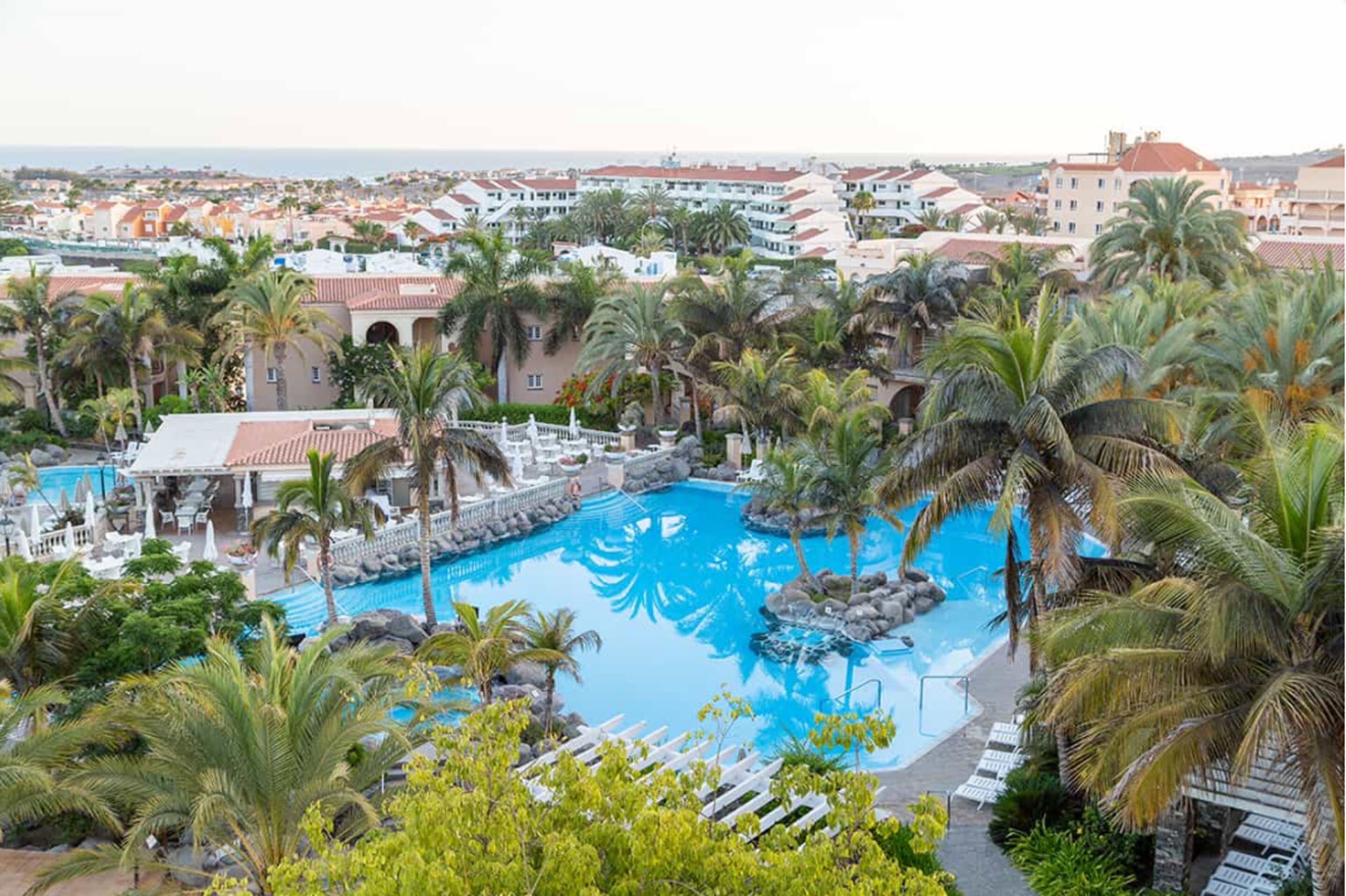 A resort with a large pool surrounded by palm trees and a view of the ocean.