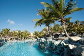 A pool surrounded by palm trees and rocks, with clear blue water and a sunny sky. - Palm Oasis Maspalomas (San Bartolomé de Tirajana)