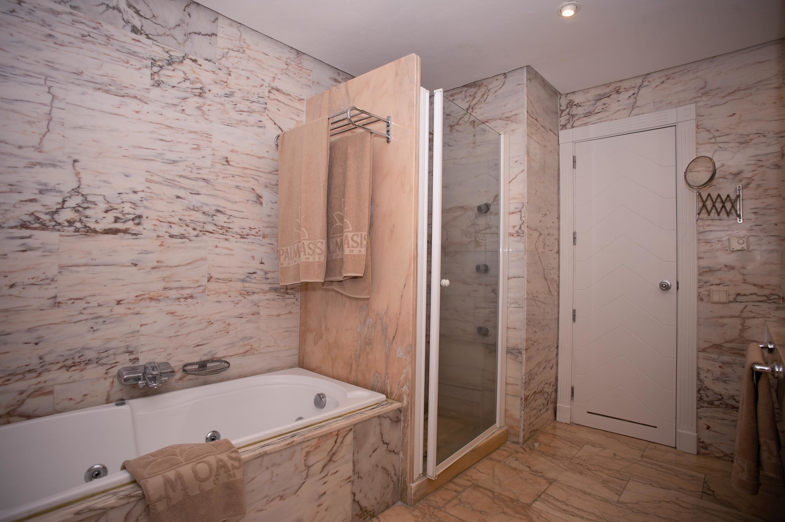 A bathroom with a marble wall, a bathtub, a shower with a glass door, and a towel rack.
