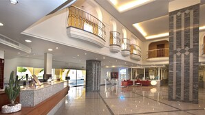 A spacious lobby with a marble reception desk, a red seating area, and a high ceiling with decorative railings. - Palm Oasis Maspalomas (San Bartolomé de Tirajana)