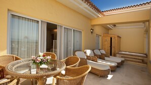 A sunlit outdoor seating area with wicker furniture, a glass-top table, and a view through large sliding doors. - Palm Oasis Maspalomas (San Bartolomé de Tirajana)