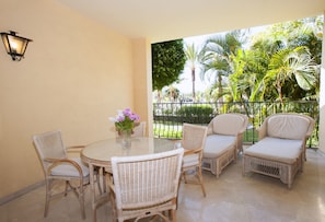 A balcony with wicker furniture, a glass table, and a vase of flowers.