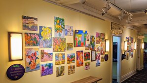 A hallway with a series of colorful paintings on the walls, a wooden bench, and a trash can. - Murray Hotel (Mackinac Island)