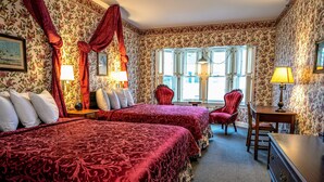 A hotel room with two beds, floral wallpaper, a red chair, a desk, and a window with shutters. - Murray Hotel (Mackinac Island)