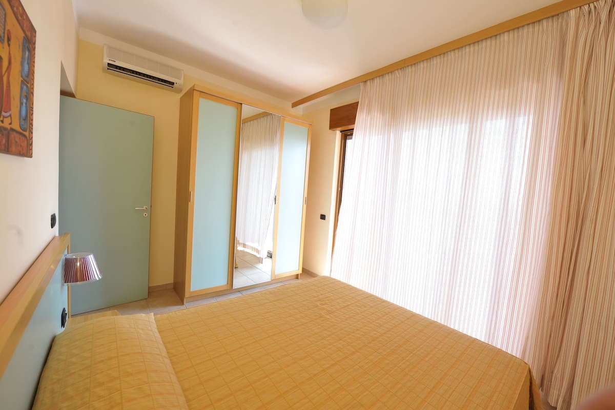 Un dormitorio con cama, armario, espejo y ventana con cortinas.