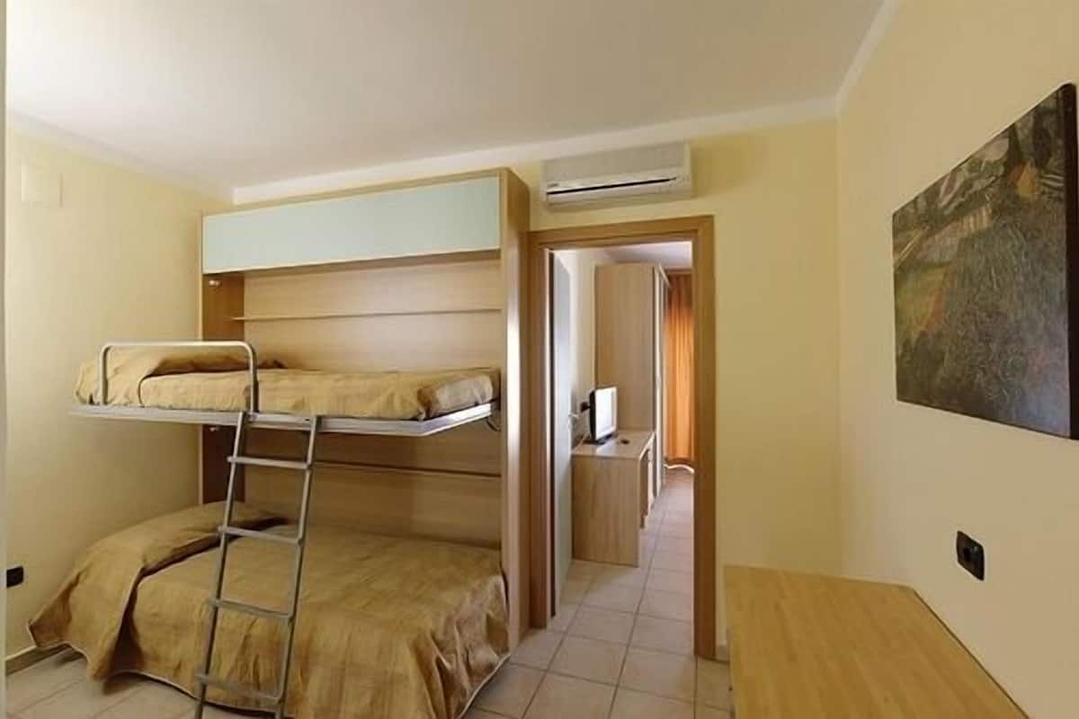 Una habitación pequeña con literas, una escalera, un aire acondicionado, un escritorio pequeño y un cuadro en la pared.