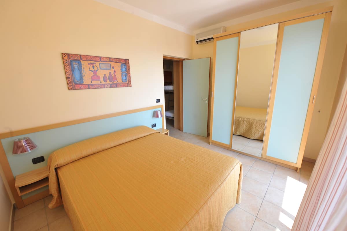 Un dormitorio con una cama, una lámpara de noche, un armario y un cuadro en la pared.