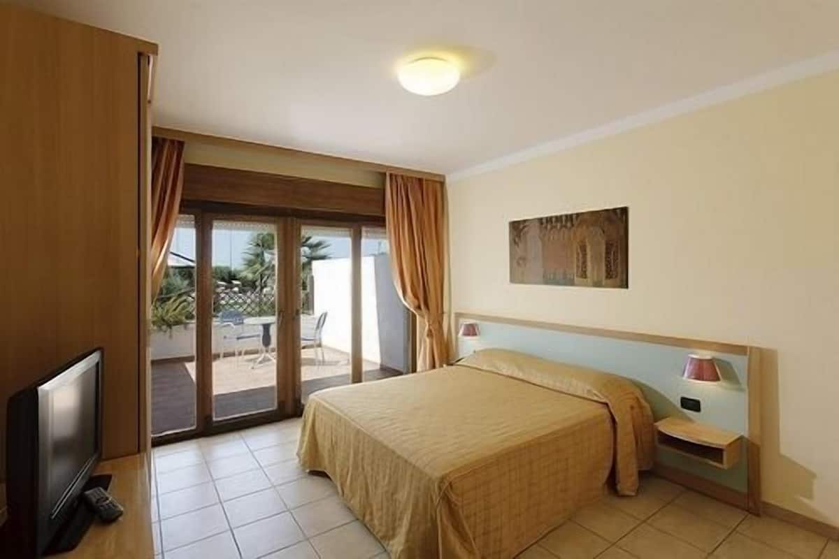 Habitación de hotel con una cama, televisor, mesita de noche y puerta corrediza de vidrio que da a un espacio exterior.