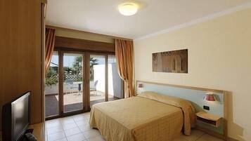 Una camera d'albergo con un letto, una televisione, un comodino e una porta scorrevole in vetro che dà su uno spazio all'aperto.