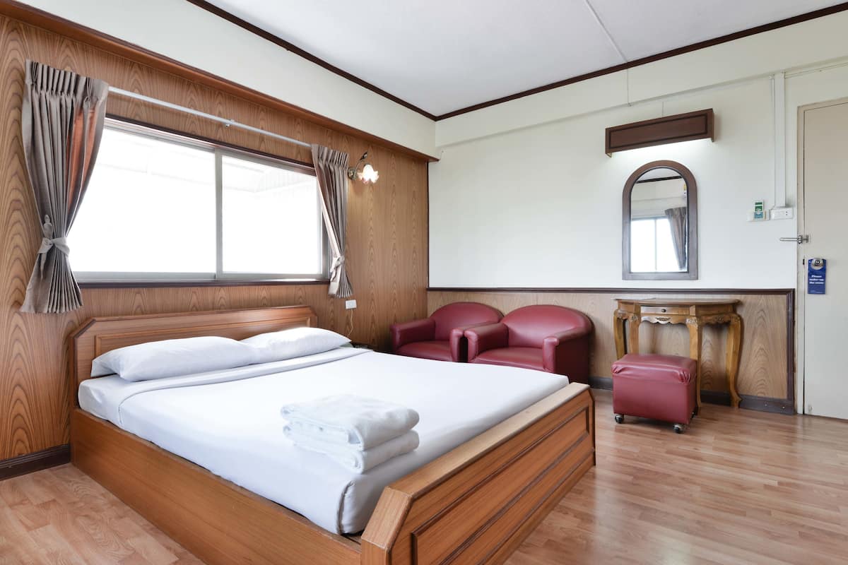 Hotellihuoneessa on puinen sänky, punainen nahkainen nojatuoli, pieni pöytä ja seinällä peili.
