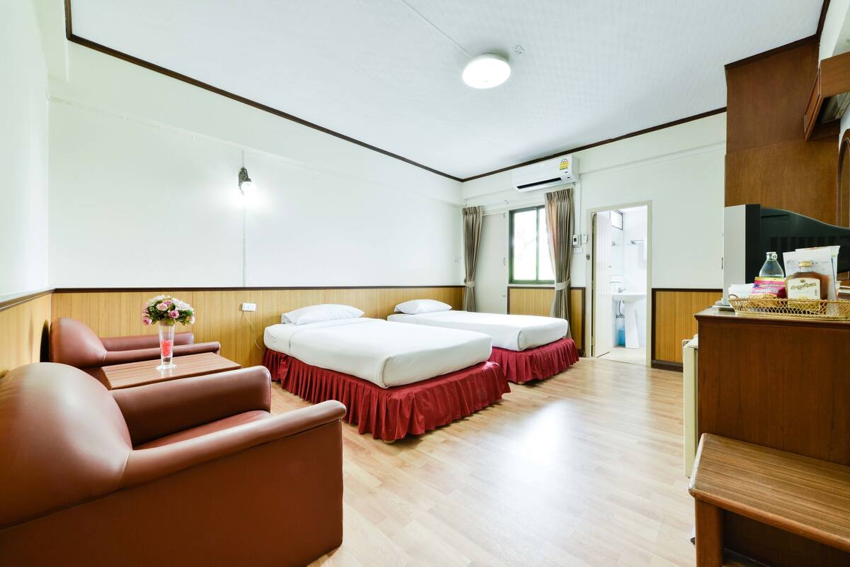Hotellihuone, jossa on kaksi sänkyä, sohva, työpöytä ja kylpyhuone, joka näkyy avoimesta ovesta.