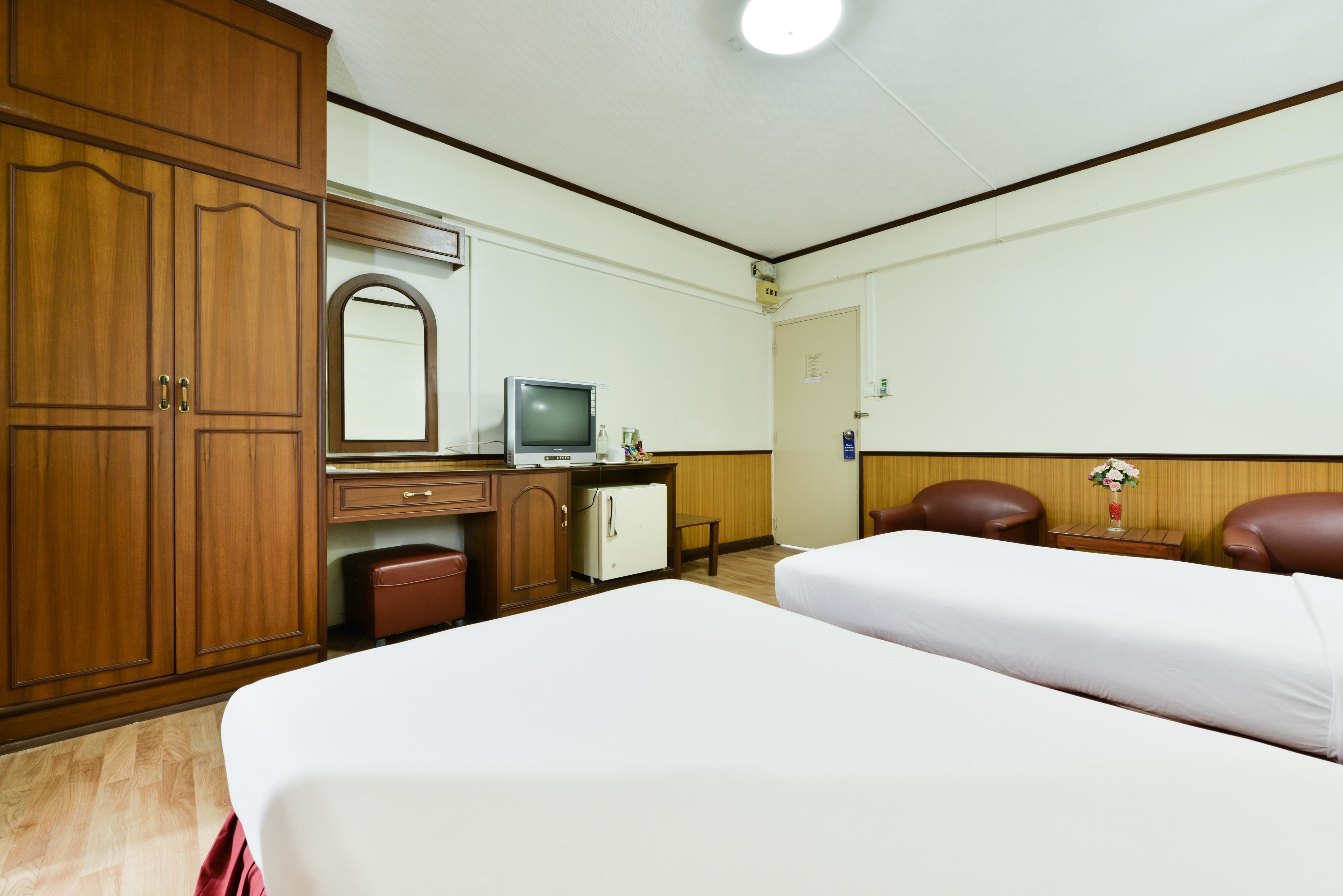 Una habitación de hotel con dos camas, un armario de madera, un escritorio con televisor y un refrigerador pequeño.