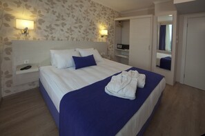 A neatly made bed with white and blue bedding, a bedside table with a phone, and a wall-mounted light fixture. - Walk In Hotel (Izmir)