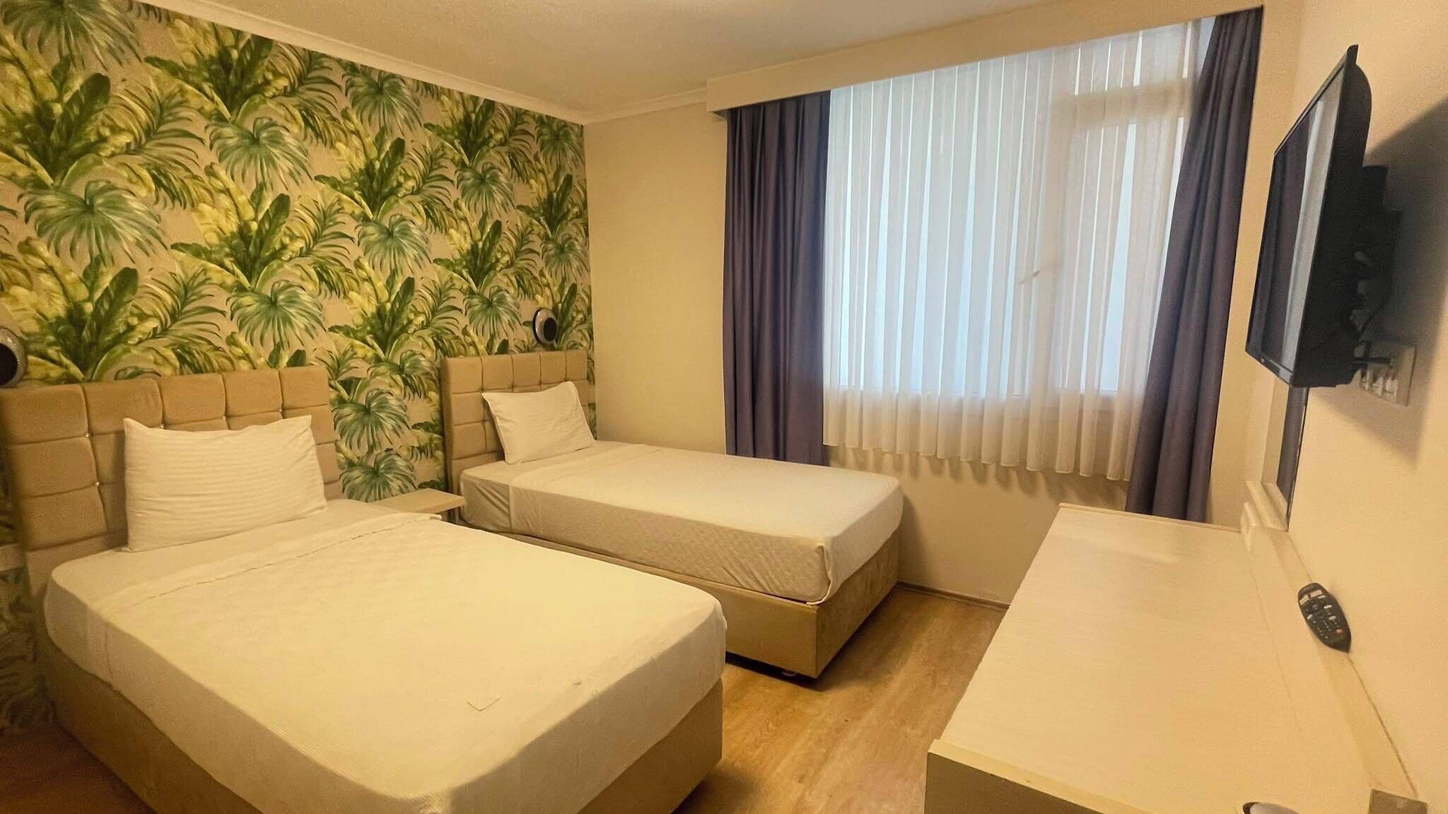 A hotel room with two beds, a desk, a television, and a window with curtains.