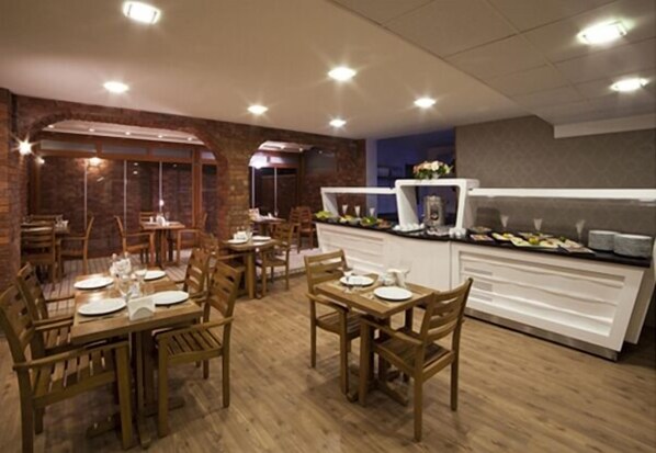 A restaurant with wooden tables and chairs, a buffet counter, and brick walls. - Walk In Hotel (Izmir)