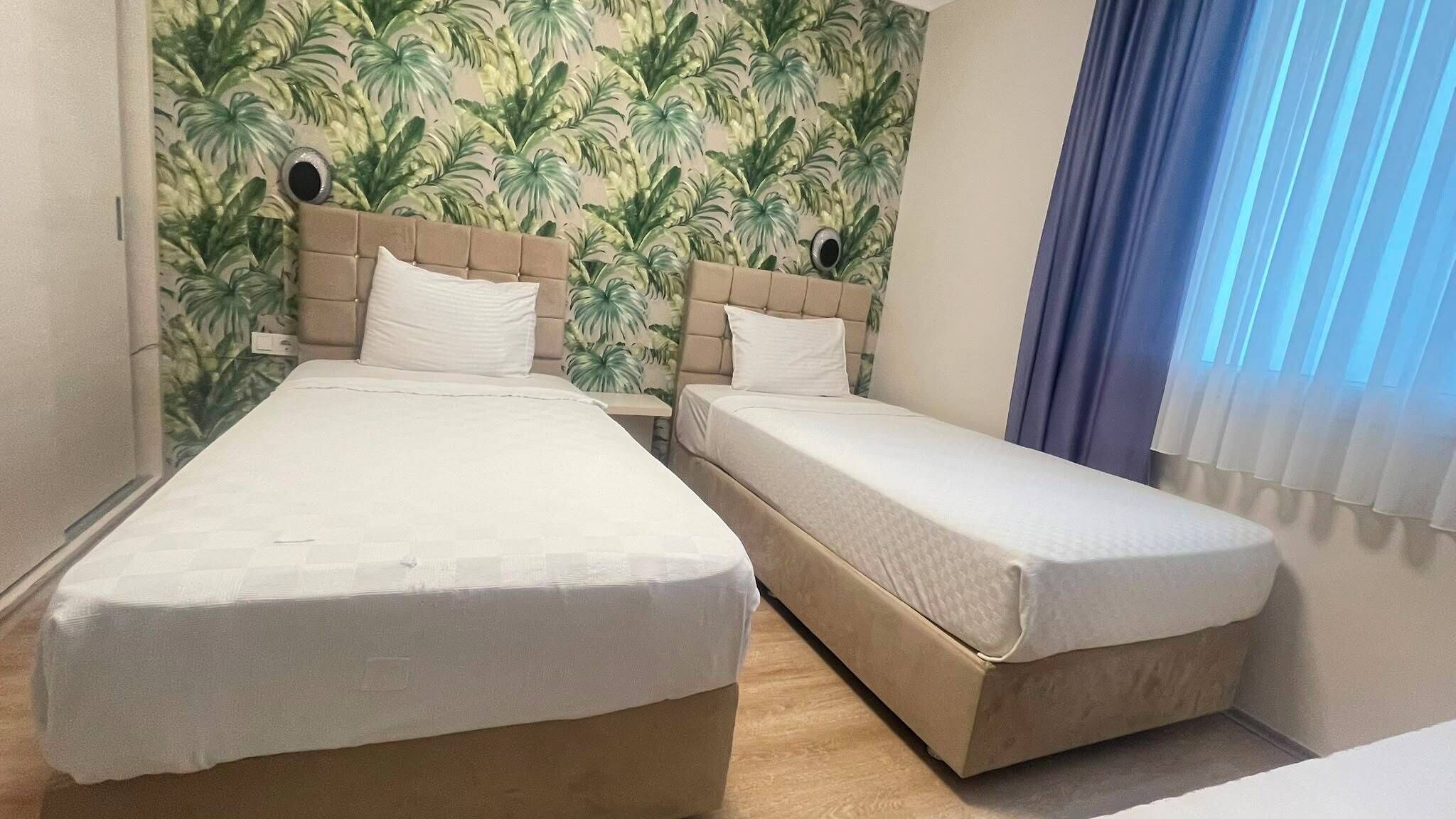 Habitación con dos camas, cabecera con diseño de hojas y ventana con cortinas.