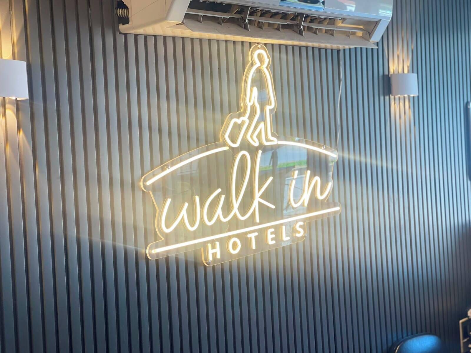 A neon sign with the text 'walk in HOTELS' against a striped wall.