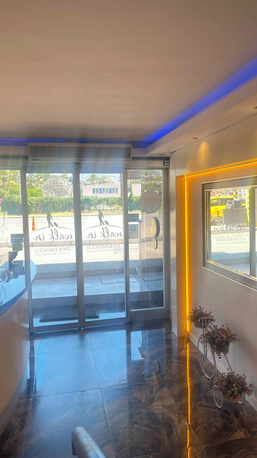 Un'ampia vetrata illumina l'ingresso della hall dell'hotel, con pavimento piastrellato e un quadro appeso alla parete.