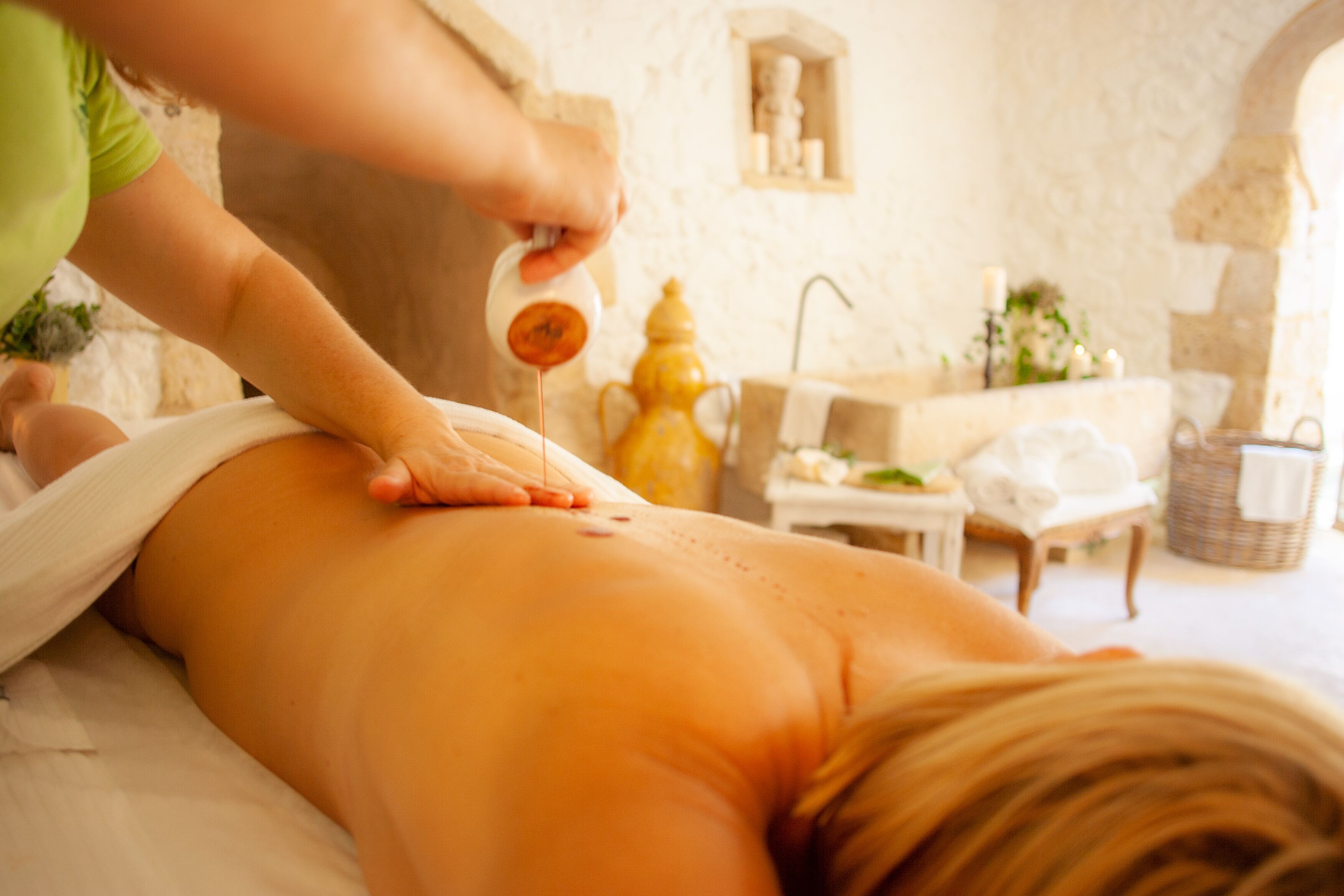 A massage therapy session in a spa setting with a stone wall and a yellow oil dispenser.