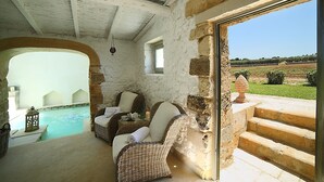 Una habitación con paredes de piedra, piscina, muebles de mimbre y vistas al campo.