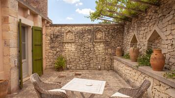 A stone-walled patio with wicker furniture, terracotta pots, and a pergola.