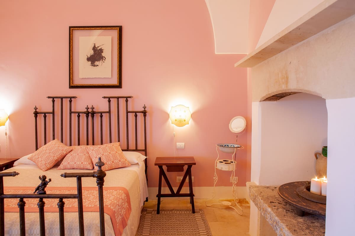 A bedroom with a bed, bedside table, wall-mounted light, and a fireplace.