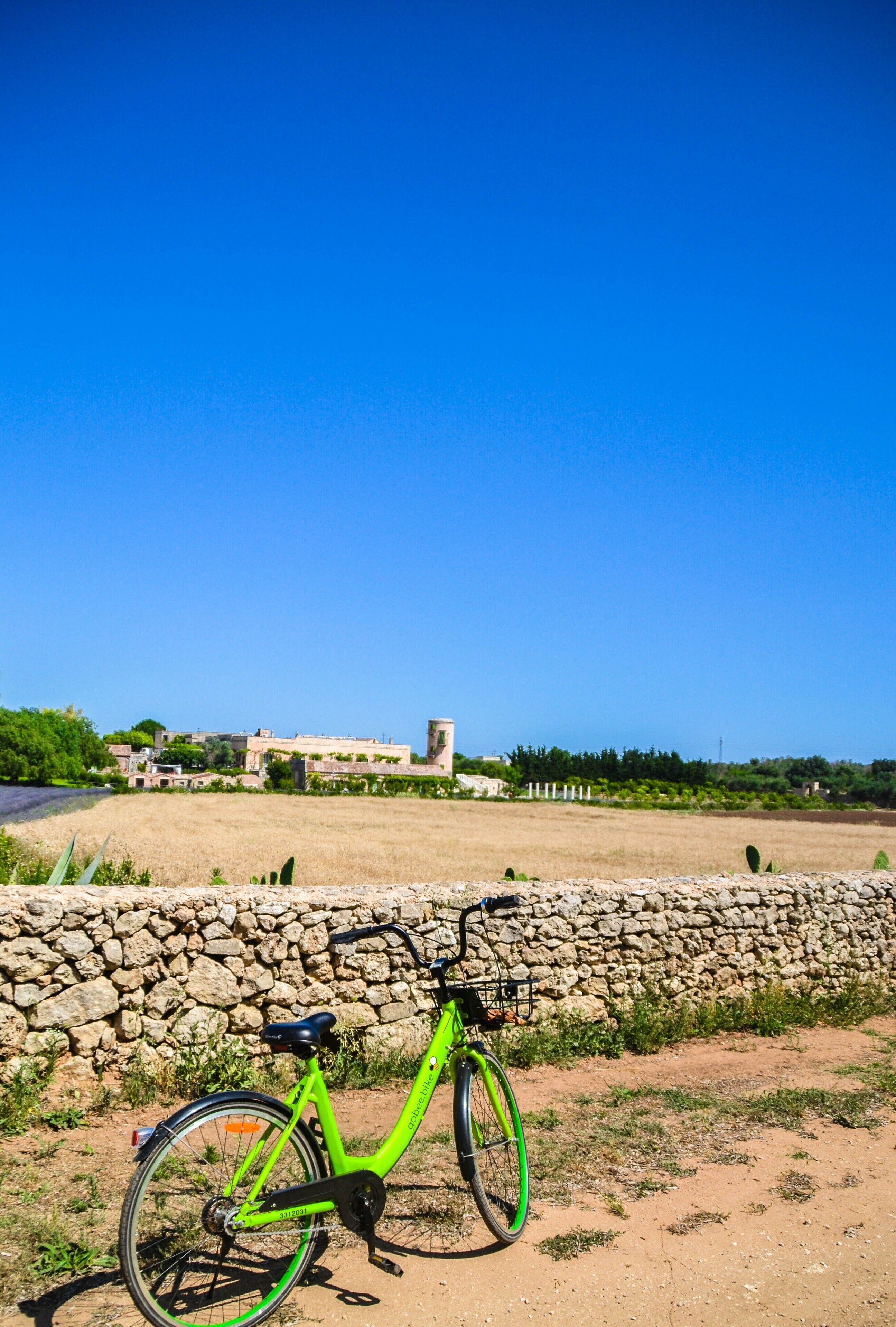 Una bicicleta verde estacionada frente a un muro de piedra, con un cielo azul despejado al fondo.
