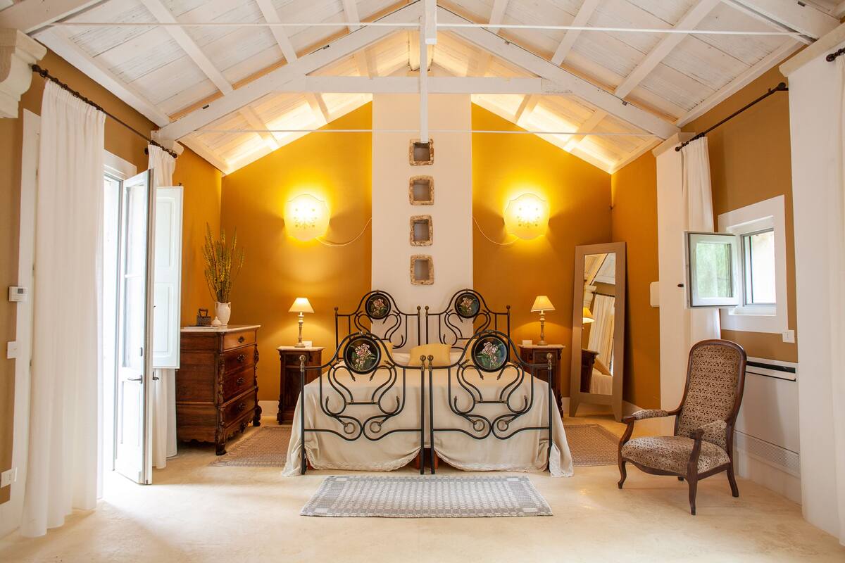 A bedroom with a bed centered under a sloped ceiling, flanked by two nightstands with lamps, a dresser, and a chair.