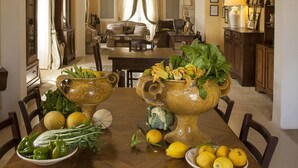 Un comedor con una mesa de madera preparada para una comida, rodeada de sillas. Hay dos jarrones grandes con flores sobre la mesa.