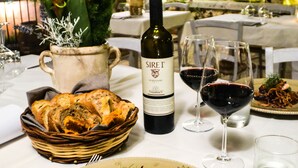 Una mesa de comedor dispuesta con una botella de Sire't, dos copas de vino, un plato de comida y una cesta de pan.