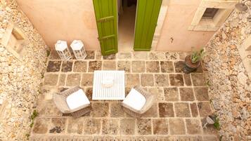 Un patio de piedra con una mesa y dos sillas de mimbre, una puerta verde y una planta en maceta.