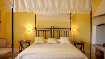 A four-poster bed with a canopy, two bedside tables, a chair, and a stone fireplace.