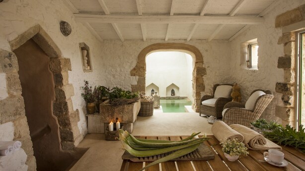 Un interior rústico con paredes de piedra, suelo de madera, mobiliario de mimbre y una pequeña zona de piscina.