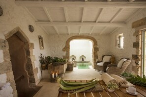 Un interior rústico con paredes de piedra, suelo de madera, mobiliario de mimbre y una pequeña zona de piscina.
