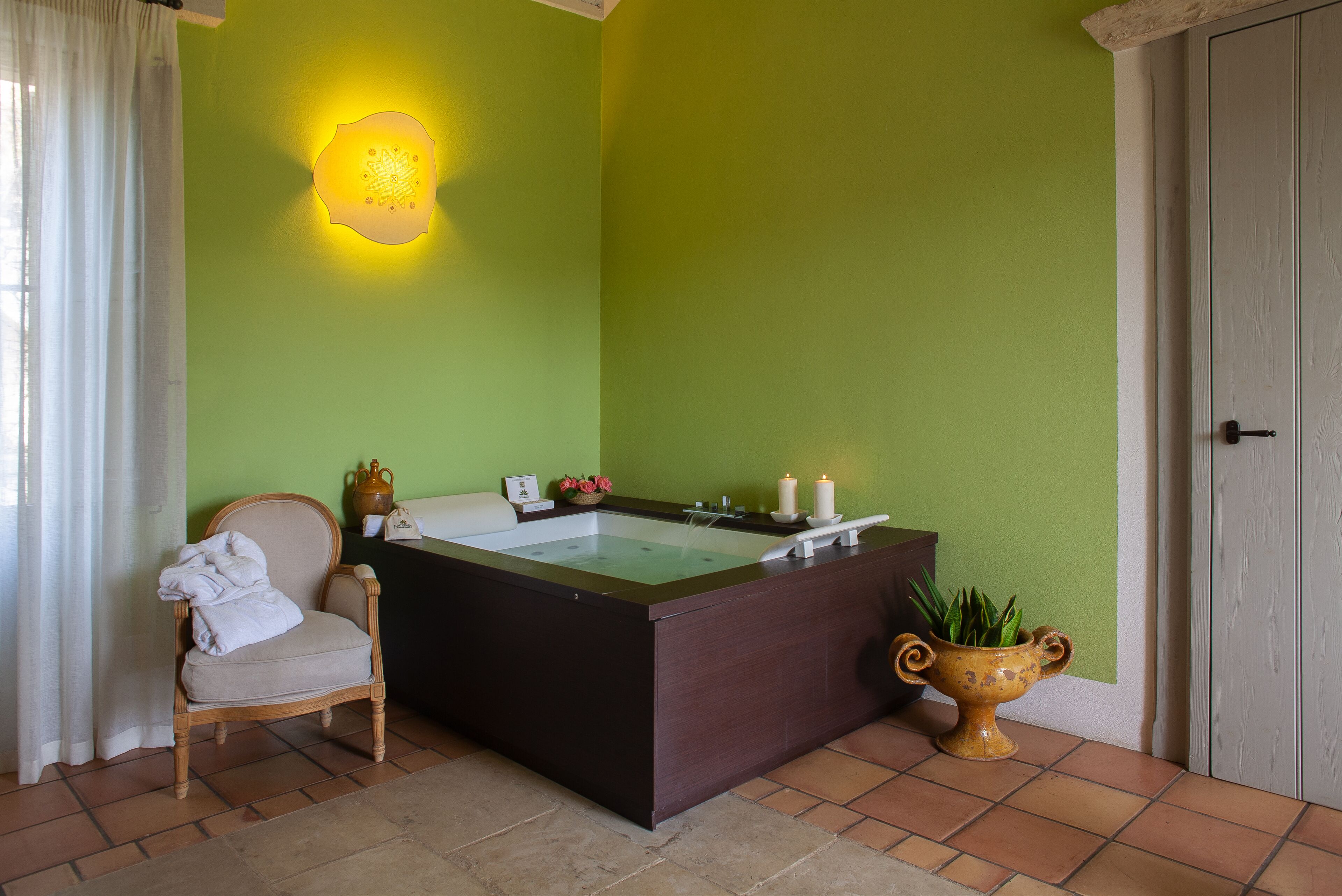 Ein Badezimmer mit Badewanne, einem Sessel und einer Wandleuchte.