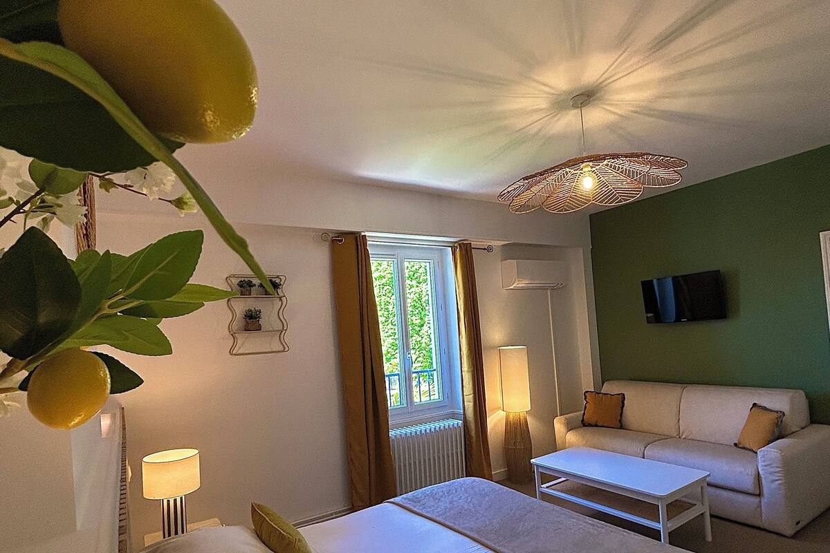 A hotel room with a bed, a sofa, a table, a TV, and a window with curtains.