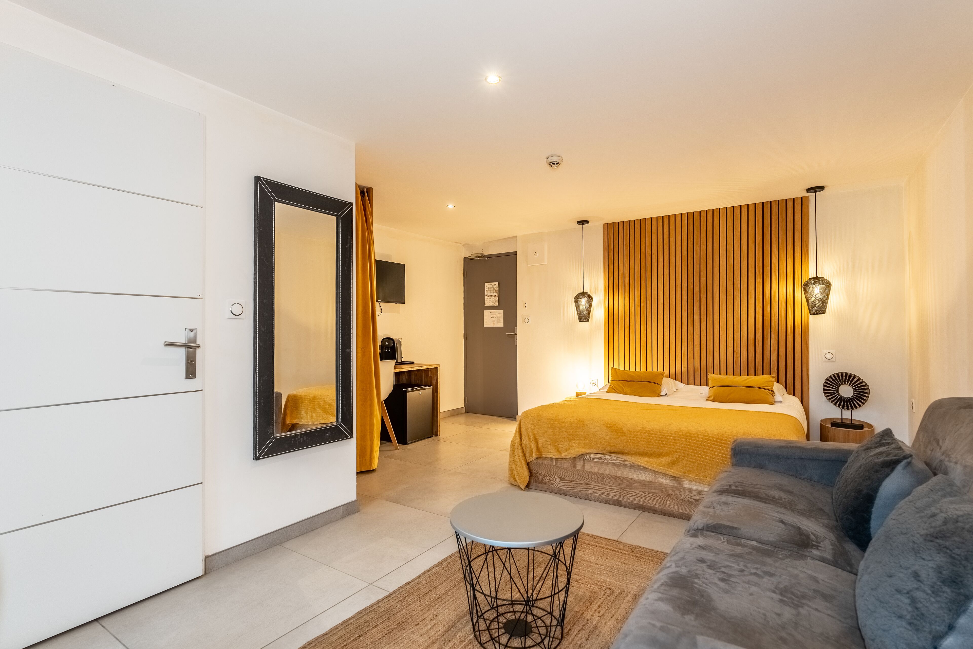 Ett modernt hotellrum med en säng, en soffa, ett litet bord och en spegel.