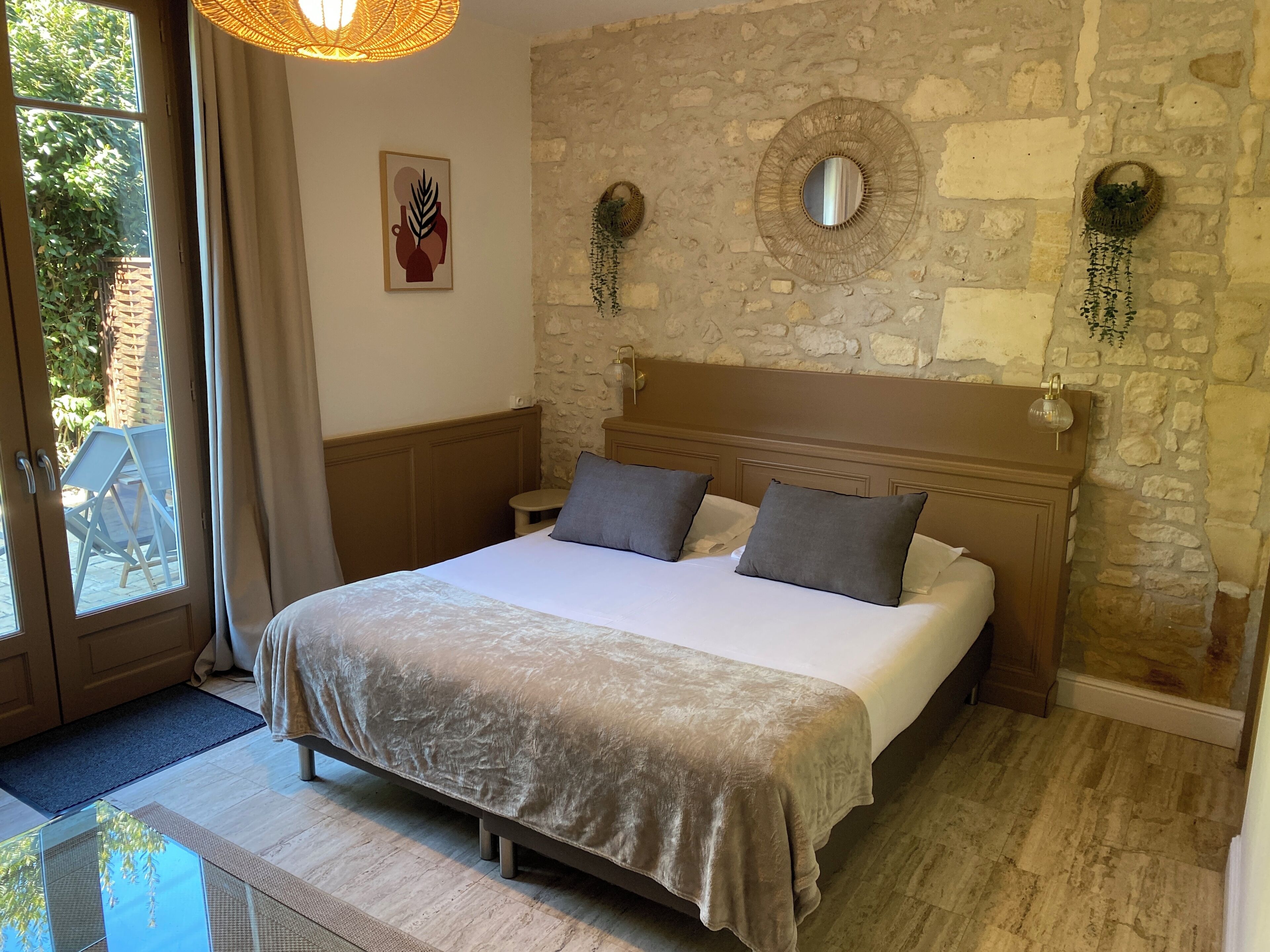 A bedroom with a stone wall, a bed with a headboard, a bedside table, and a window.