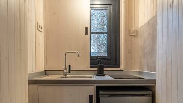 A compact kitchen with wooden walls, a window, a sink, a faucet, and a built-in dishwasher.