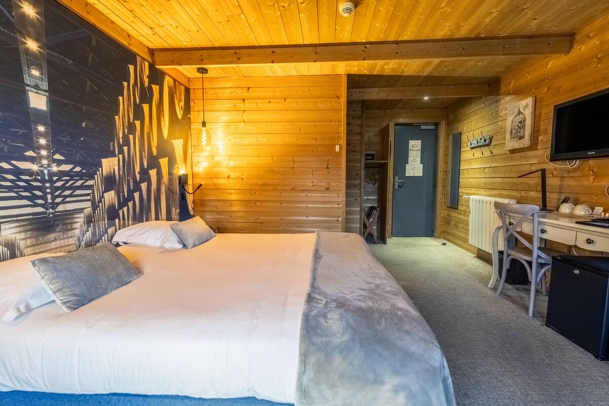 A wooden cabin bedroom with a bed, a desk, and a television.