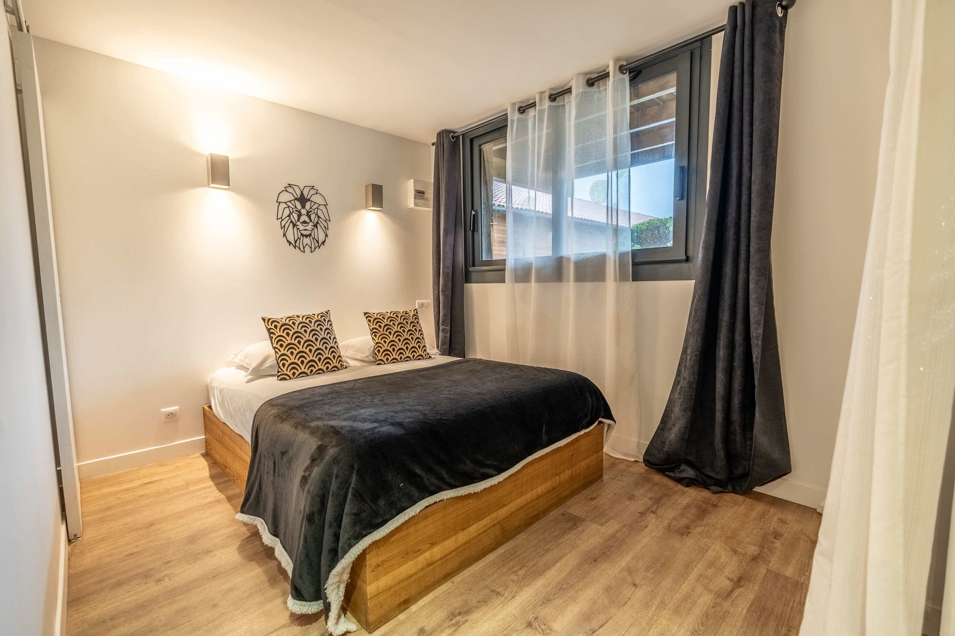 A bedroom with a wooden bed, patterned pillows, a black blanket, and a window with curtains.