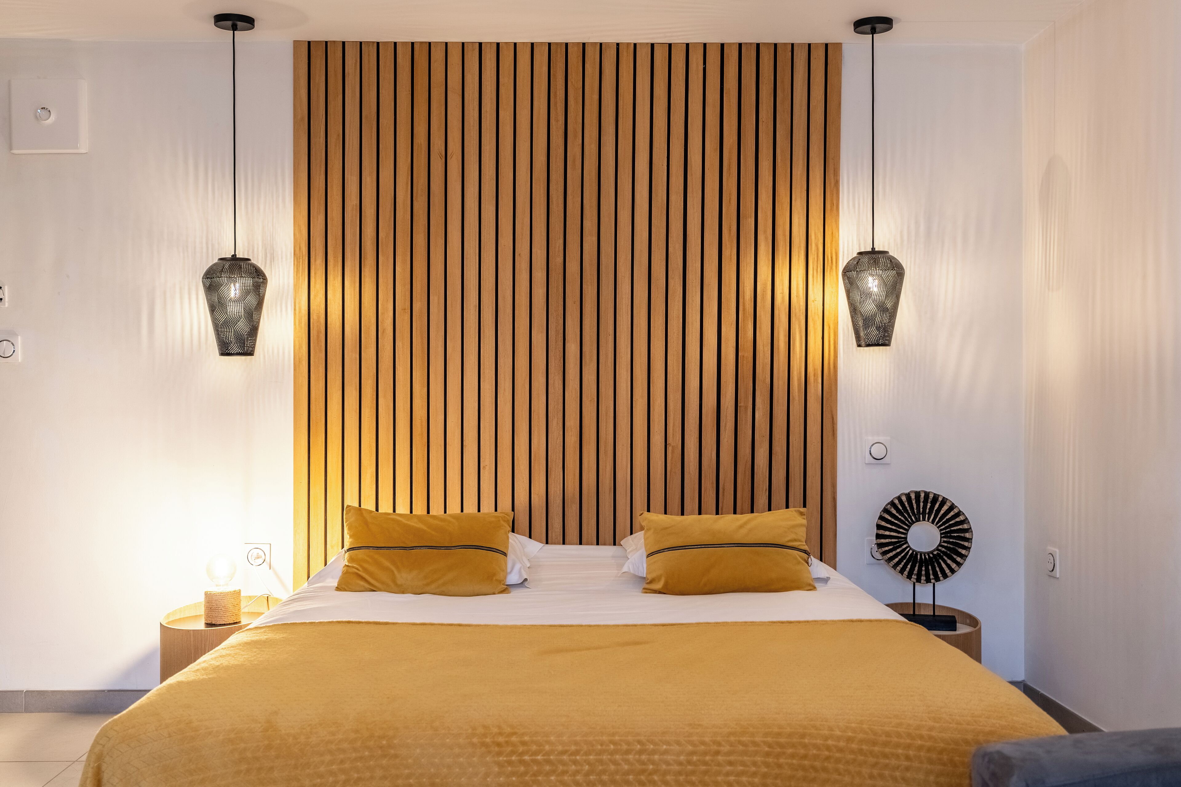 Una habitación de hotel moderna con una cama grande, dos lámparas de noche y un panel de pared de madera.