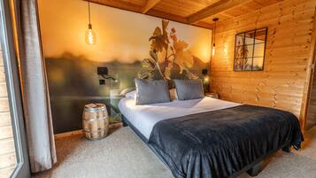 A wooden cabin bedroom with a bed, pillows, a nightstand, a barrel, and a wall-mounted light fixture.