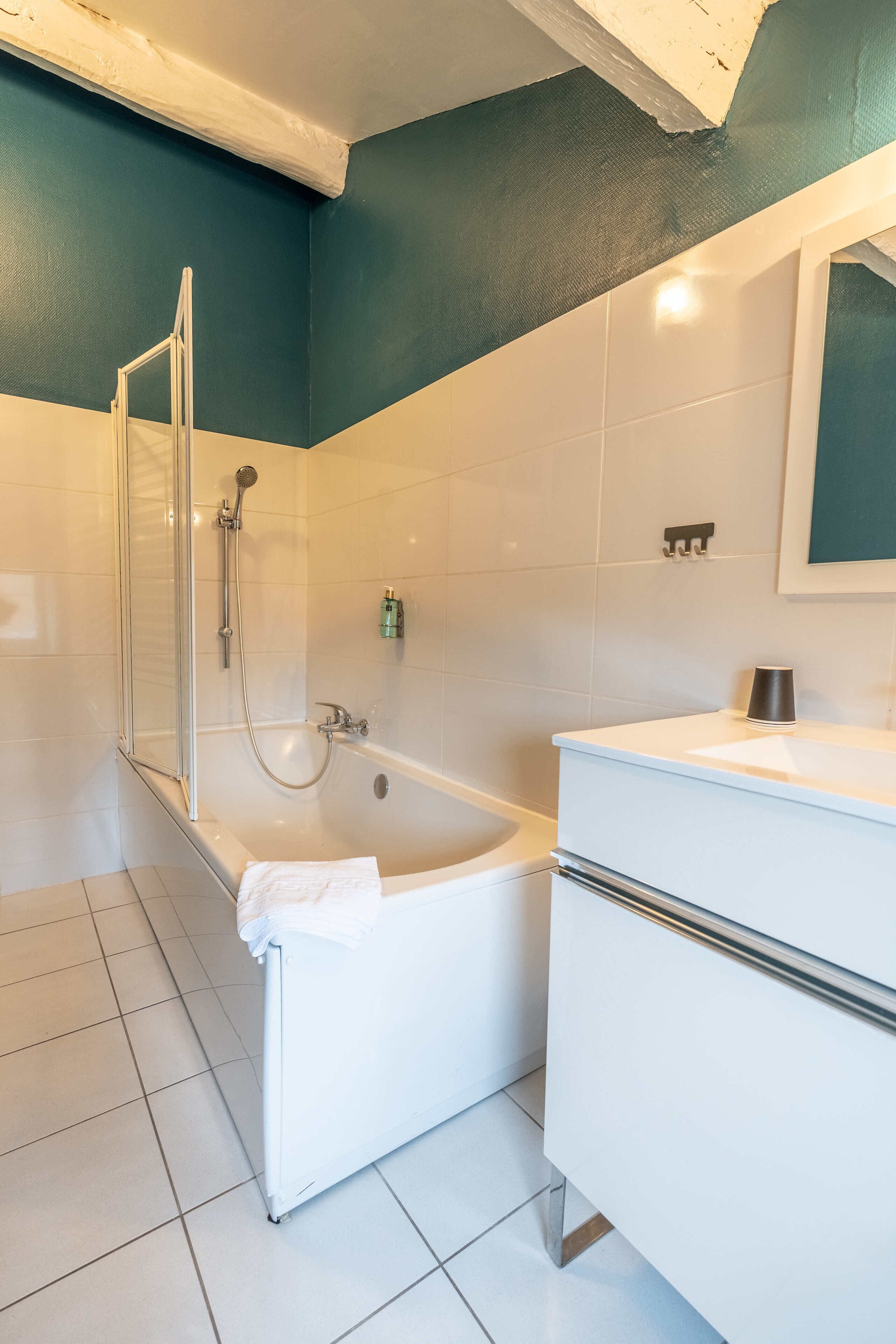 A modern bathroom with a glass shower enclosure, a white bathtub, and a white vanity with a mirror.