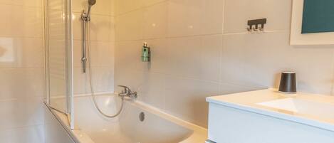 A modern bathroom with a glass shower enclosure, a white bathtub, and a white vanity with a mirror.